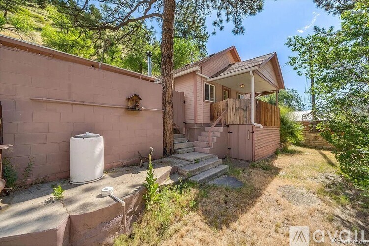 A house with a pink exterior is surrounded by trees and has a water heater outside.