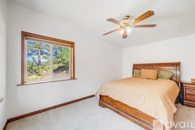 A bedroom with a bed, a ceiling fan, and a window overlooking a forest.