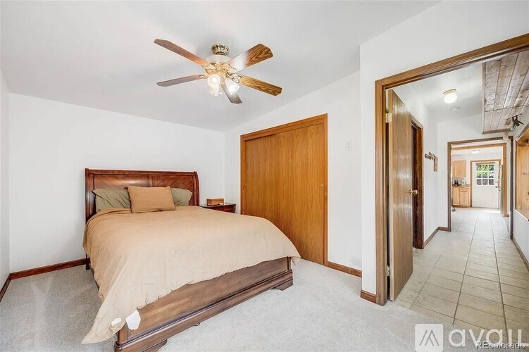 A bedroom with a bed, a ceiling fan, and a door leading to another room.