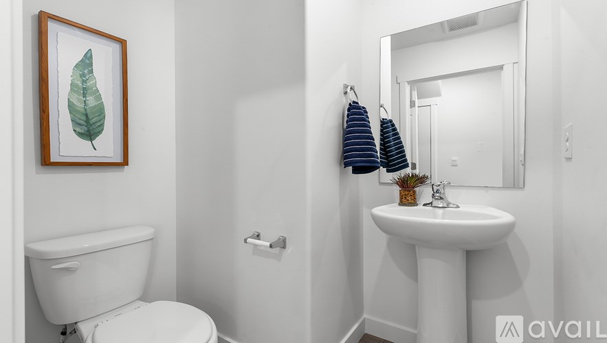 A white bathroom with a toilet, sink, and a leaf picture on the wall.