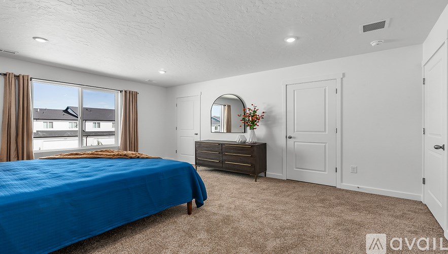 A bedroom with a large bed, a dresser, and a window overlooking a street.