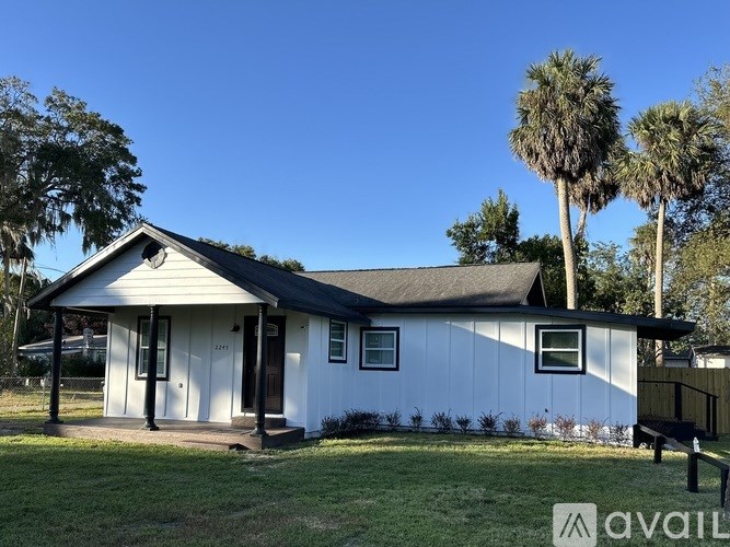 A white house with a black roof is surrounded by green grass and palm trees.
