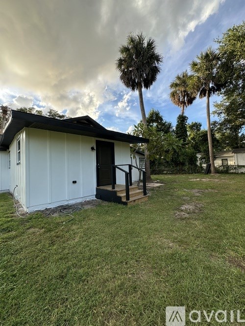 A small white building with a black roof is surrounded by grass and palm trees.