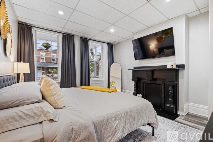 A bedroom with a large bed, a fireplace, and a flat-screen TV mounted above it.