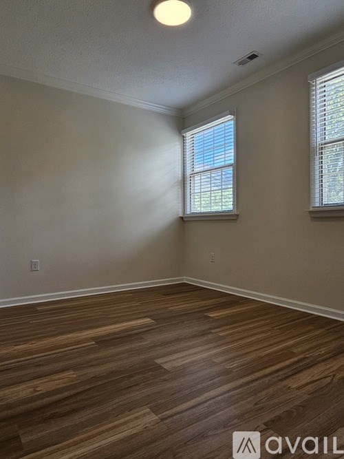 A room with wooden flooring and two windows.