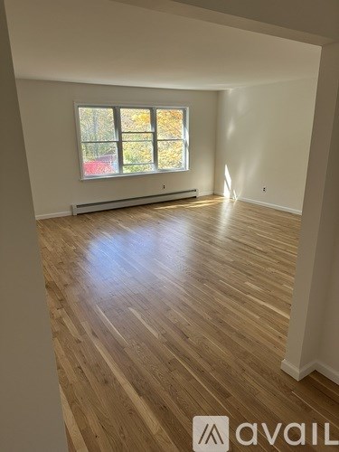 A room with wooden flooring and a window with autumn leaves visible outside.