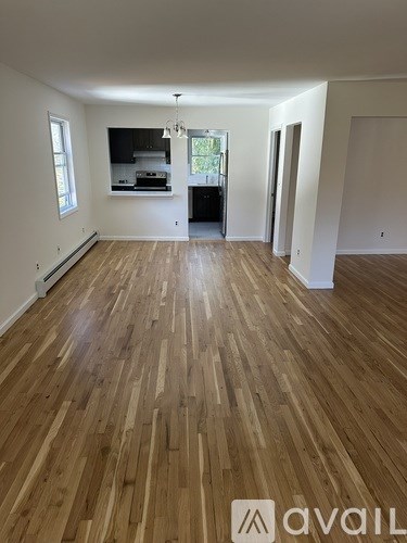 A room with wooden flooring and a kitchen area in the background.