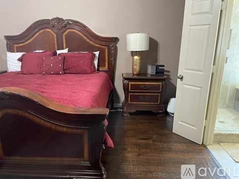 A bedroom with a large bed and a small table with a lamp on it.