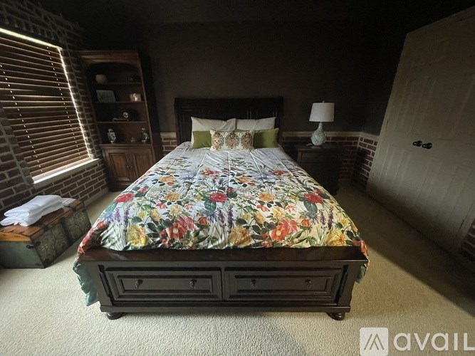 A bed with a floral comforter is in the center of a room with a wooden cabinet and a lamp.