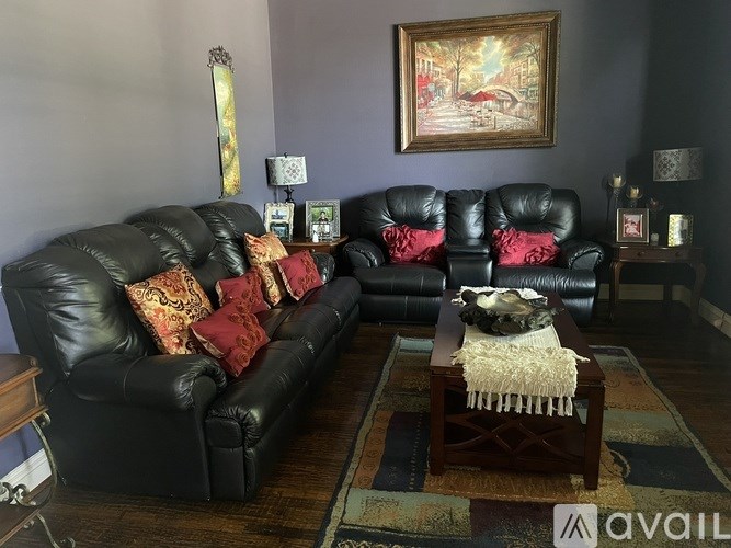 A black leather couch with red pillows and a wooden coffee table in front of it.