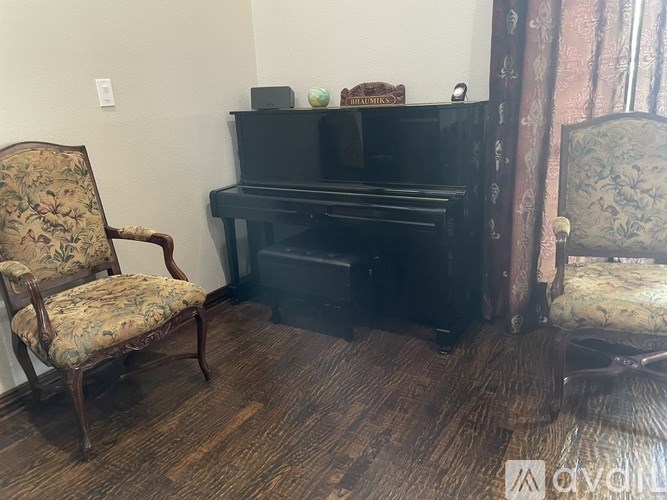 A black piano sits between two ornate chairs in a room with wood flooring.
