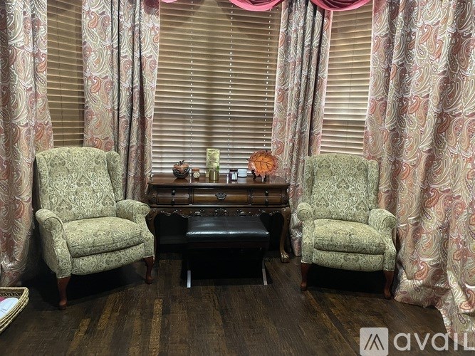 Two chairs and a table are in front of patterned curtains.