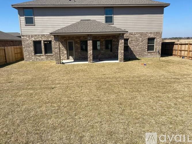 A house with a grey roof and a stone wall is surrounded by a fence and a grassy yard.