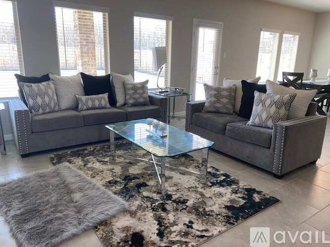 A living room with a grey couch, a glass coffee table, and a rug.