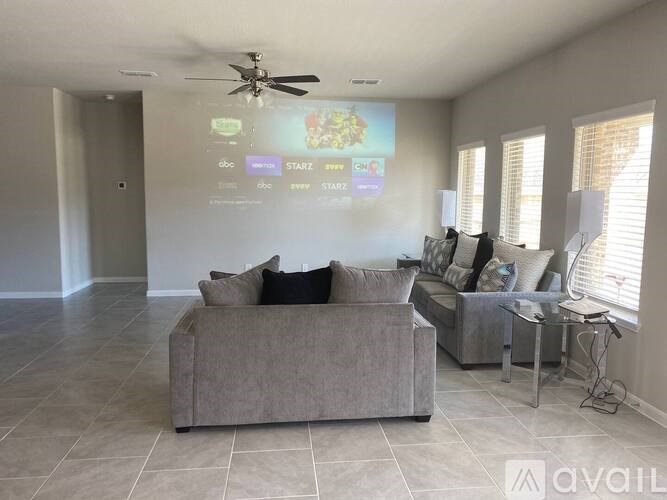 A living room with a grey couch and a projector screen showing a menu.