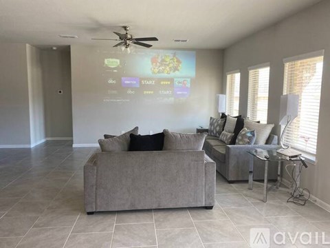 A living room with a grey couch and a projector screen showing a menu.