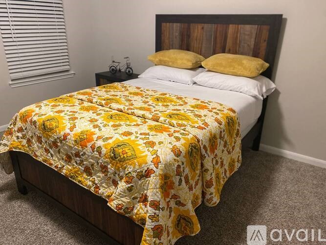 A bed with a yellow and white comforter is in a room with a wooden headboard.