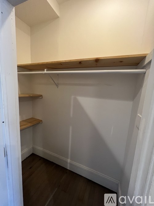 A white closet with a wooden shelf and a white door.