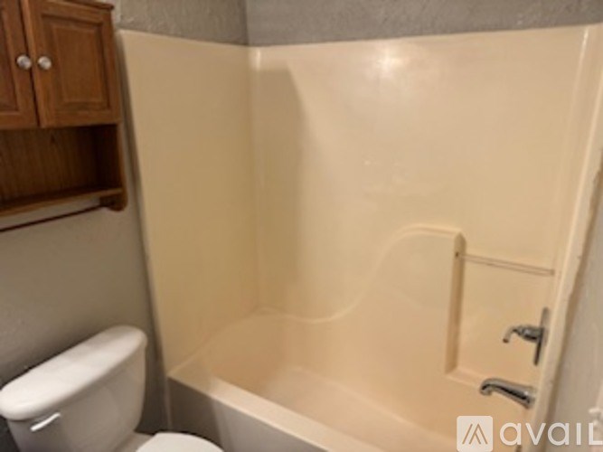 A bathroom with a toilet, tub, and wooden cabinet.