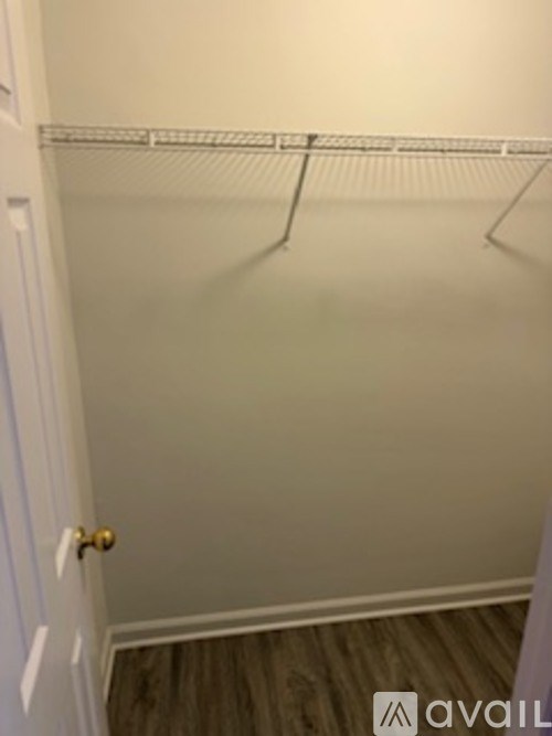 A white door with a gold handle is on the left side of a room with a white wall and a white shelf.