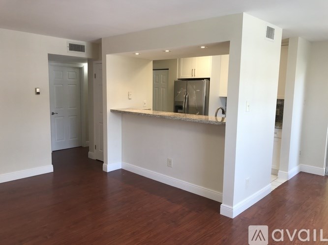 A spacious living room with hardwood floors and a kitchenette in the background.