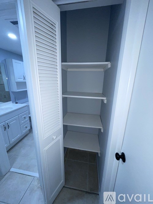 A white pantry with a door open to a darker room.