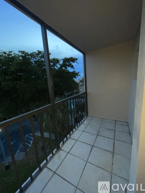 A balcony with tiled flooring and a metal railing overlooks a parking lot and trees.