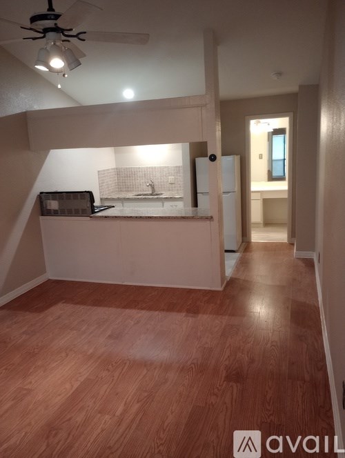 A room with wooden flooring and a kitchenette in the corner.