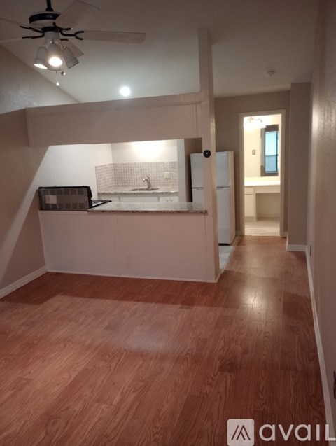 A room with wooden flooring and a kitchenette in the corner.