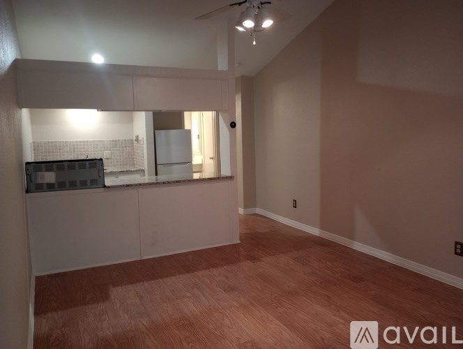 A room with wooden flooring and a kitchen area with white appliances.