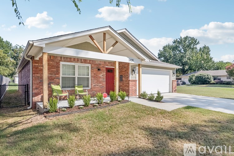 A house with a red door and a white garage door is surrounded by a lawn and trees.
