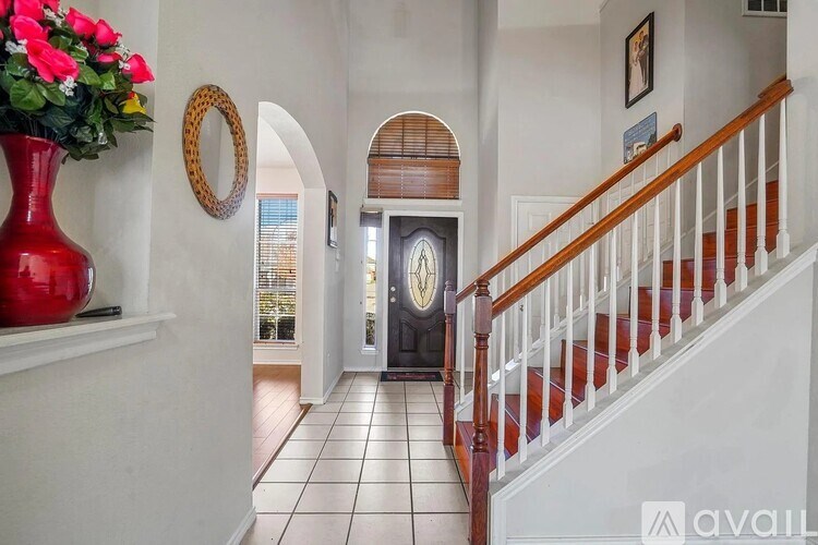 A red vase with flowers sits on a white shelf next to a staircase.