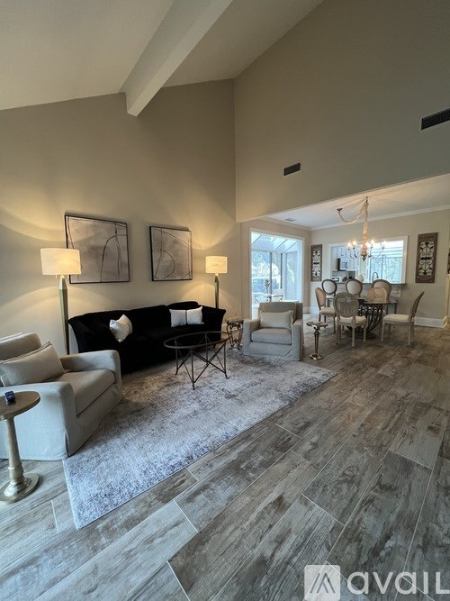 A living room with a black couch, a grey armchair, a small table with a lamp, and a chandelier.