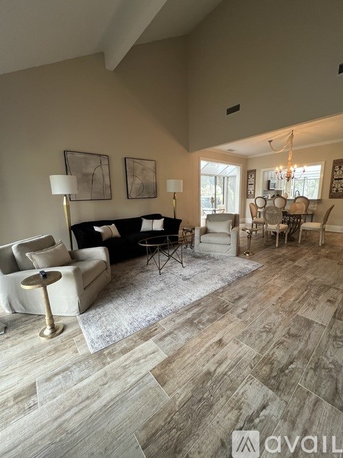 A living room with a black couch, white armchairs, and a wooden floor.