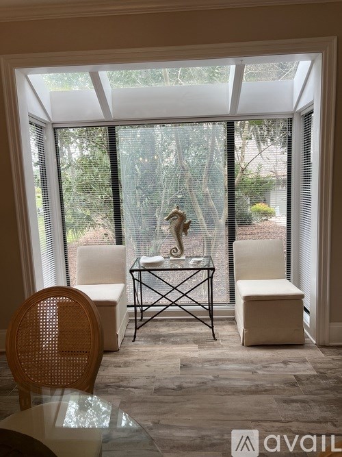 A room with a glass table and chairs with a window in the background.