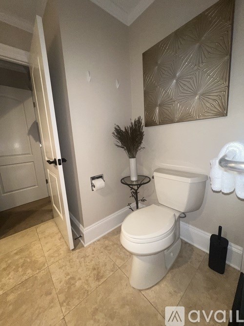 A bathroom with a toilet, a plant, and a decorative wall hanging.