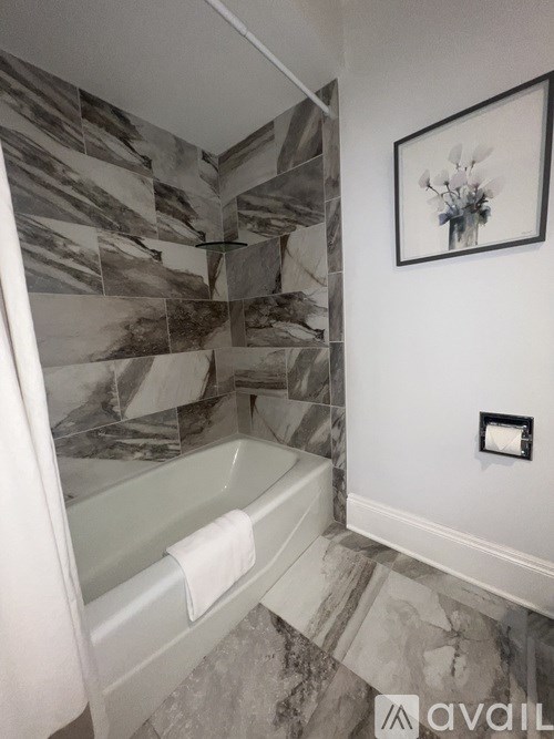 A bathroom with a marble tile wall and a white bathtub.