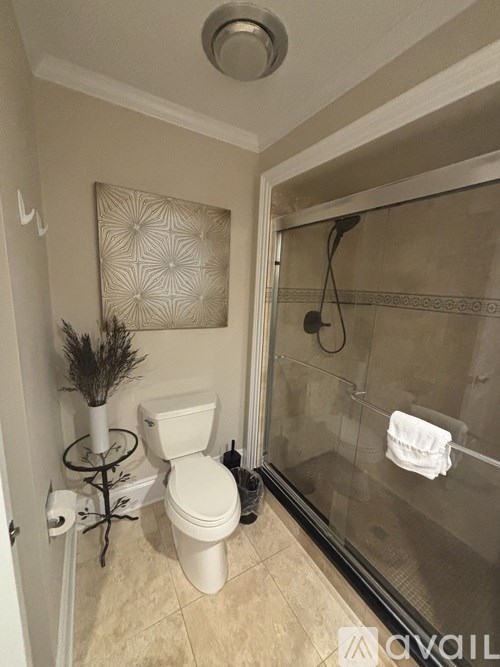 A bathroom with a toilet, a glass shower door, and a decorative wall hanging.