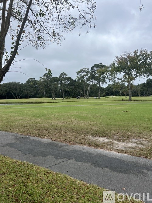 A grassy field with trees and a wet path in the foreground.