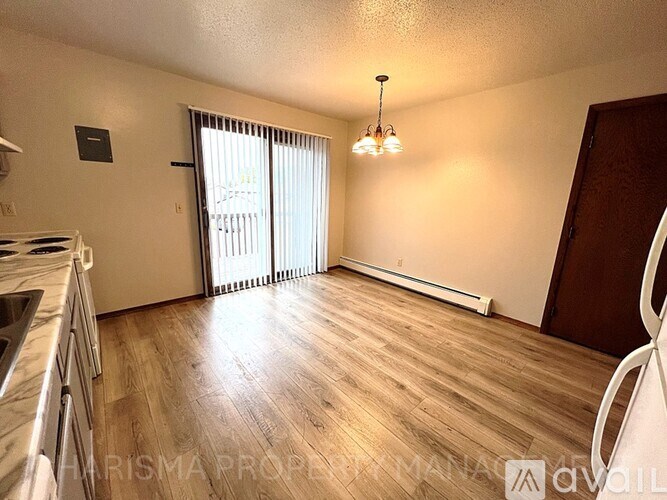 A well-lit, empty room with wooden flooring and a window with blinds.