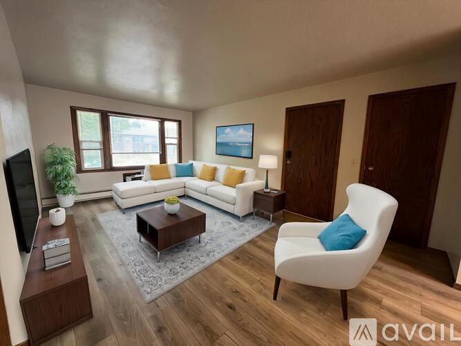 A living room with a white sofa, a white armchair, a wooden floor, and a grey rug.
