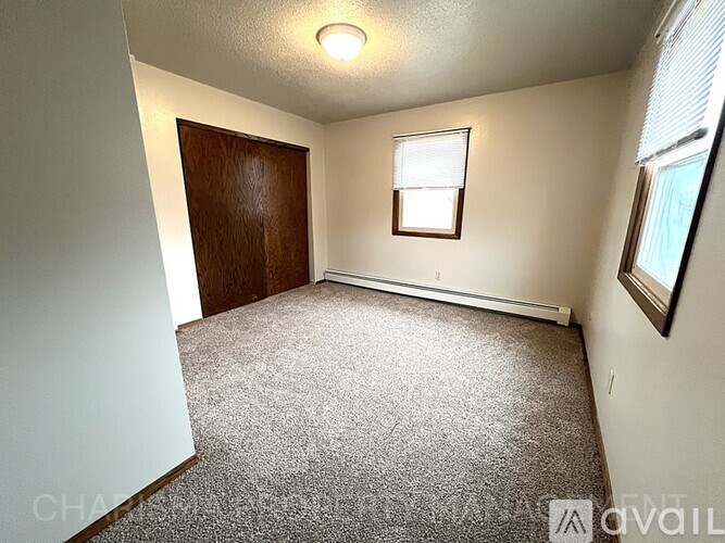 A room with a carpeted floor, a window with blinds, and a wooden door.