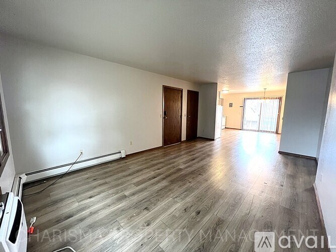 A spacious room with wooden flooring and a door on the left.