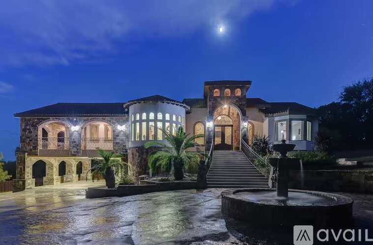 A large, well-lit house with a fountain in front at night.