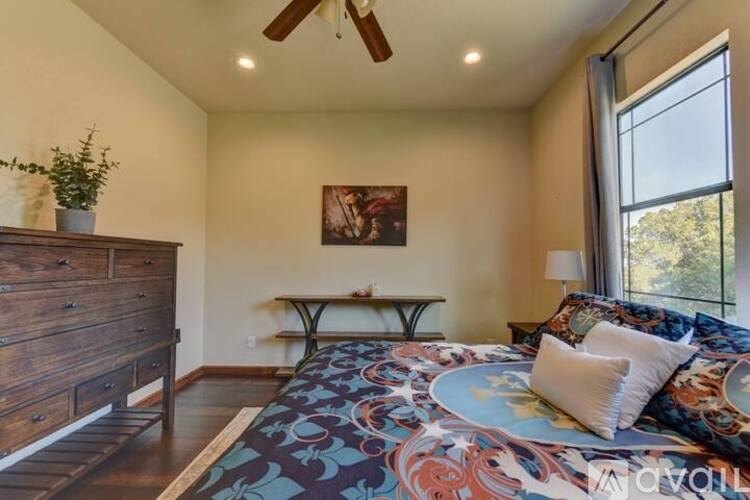 A bedroom with a bed, a dresser, a ceiling fan, and a painting on the wall.