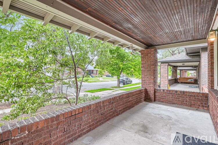A covered patio with a brick wall and a tree in the background.
