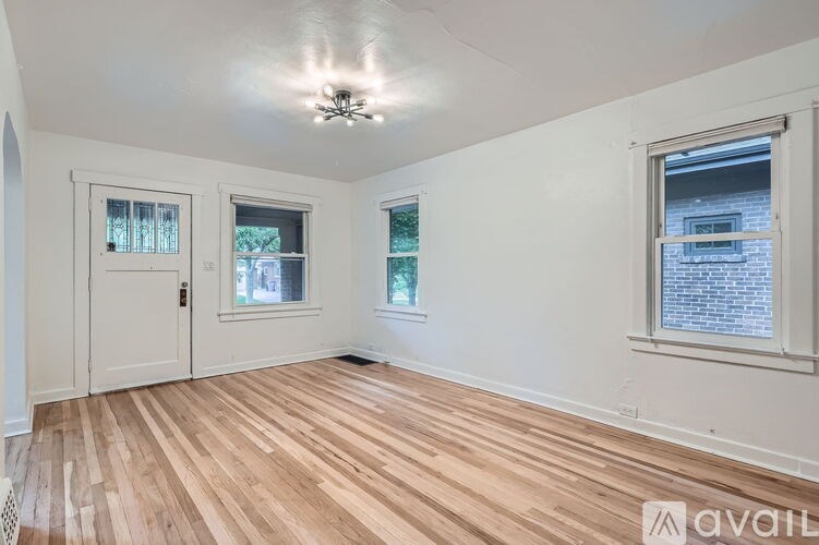 A room with wooden flooring and white walls, featuring a ceiling fan and three windows.