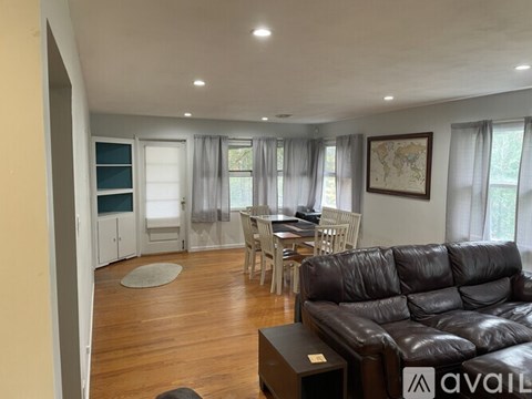 A living room with a black leather couch and a dining table with chairs.