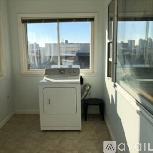A small white washing machine sits in a room with a window.