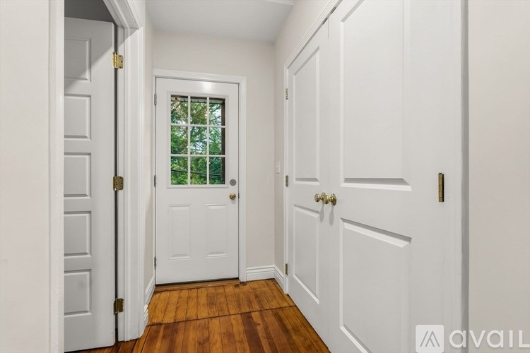 A hallway with white doors and a window with a view of trees.